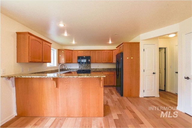 1962 E 6th St, Moscow, ID 83843 - kitchen featuring stone counters, a peninsula, light wood-style floors, brown cabinetry, and black appliances