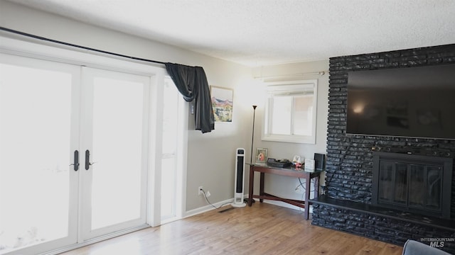 living room with french doors, a textured ceiling, a brick fireplace, and hardwood / wood-style floors