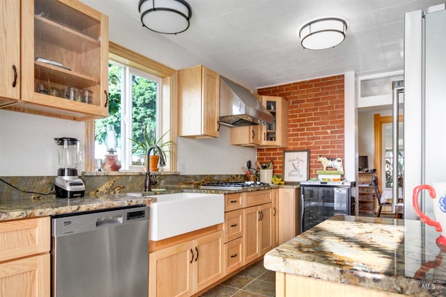 kitchen with light brown cabinetry, wall chimney range hood, brick wall, stainless steel appliances, and dark tile patterned flooring