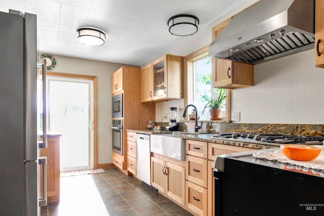 kitchen featuring appliances with stainless steel finishes, dark tile patterned floors, light brown cabinetry, and wall chimney range hood