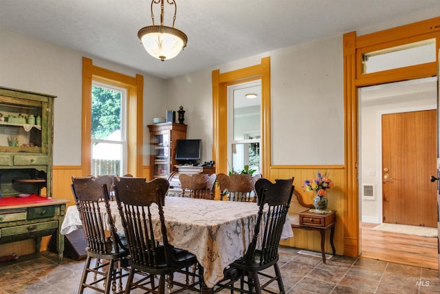 dining area featuring wood walls, stone finish floor, wainscoting, and visible vents