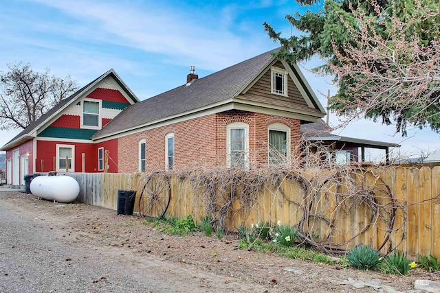 view of side of home with brick siding, fence, a shingled roof, and a chimney