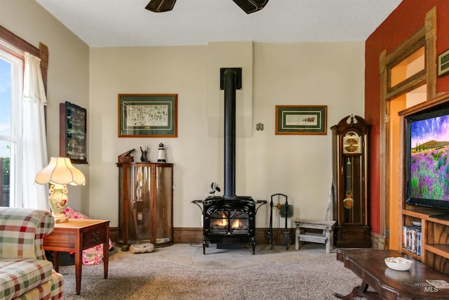 living room featuring a wood stove, a ceiling fan, and carpet