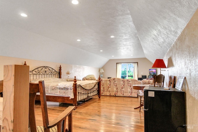 bedroom with light hardwood / wood-style flooring, a textured ceiling, and vaulted ceiling