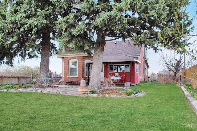 back of property with a shingled roof, brick siding, fence, and a lawn