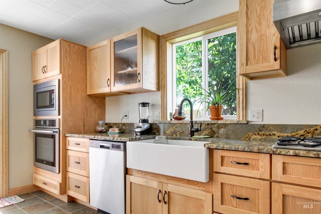 kitchen with dark tile patterned flooring, stainless steel appliances, light brown cabinetry, sink, and wall chimney exhaust hood