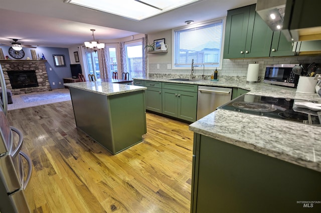 kitchen with green cabinetry, a sink, a stone fireplace, stainless steel appliances, and light wood-type flooring