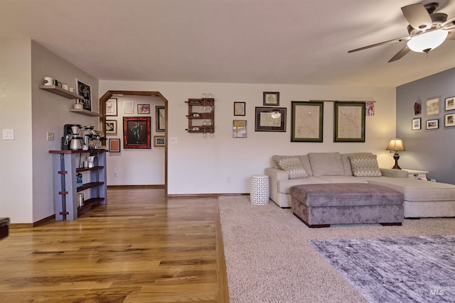 living area with baseboards, arched walkways, wood finished floors, and a ceiling fan