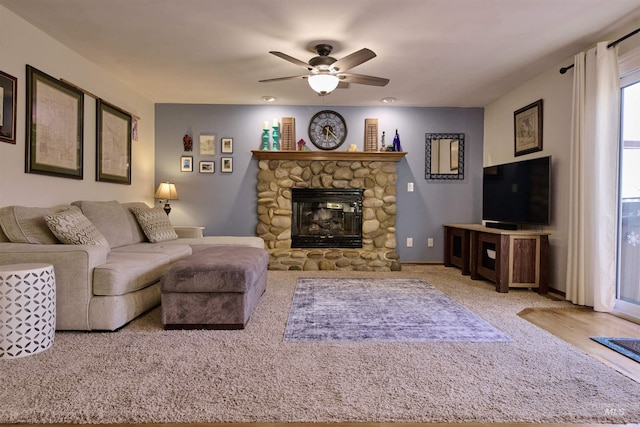 living room with a stone fireplace, carpet, baseboards, and ceiling fan