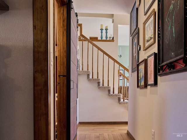 hall featuring a barn door, stairway, baseboards, and light wood finished floors