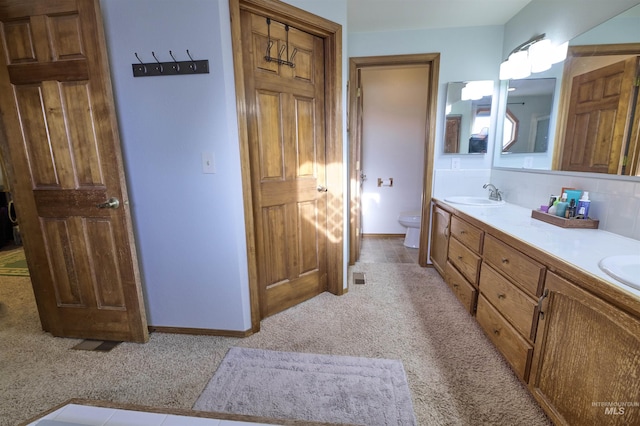 full bath featuring baseboards, double vanity, a sink, decorative backsplash, and toilet