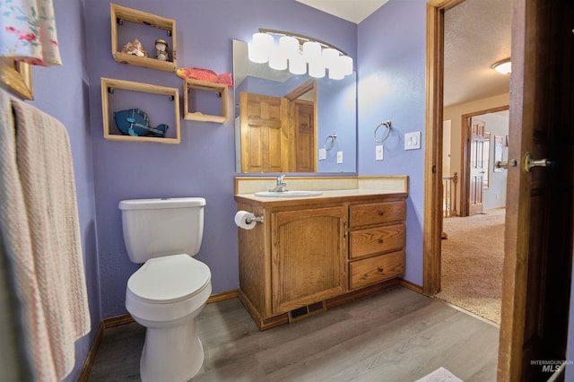 half bathroom featuring toilet, vanity, baseboards, and wood finished floors