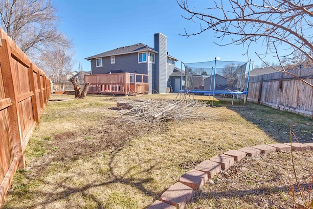 back of house with a trampoline, a fenced backyard, a chimney, and a lawn