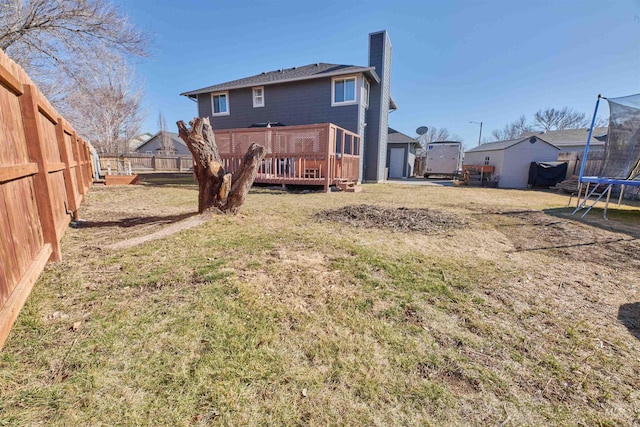 rear view of house with a fenced backyard, a chimney, a deck, a trampoline, and a lawn