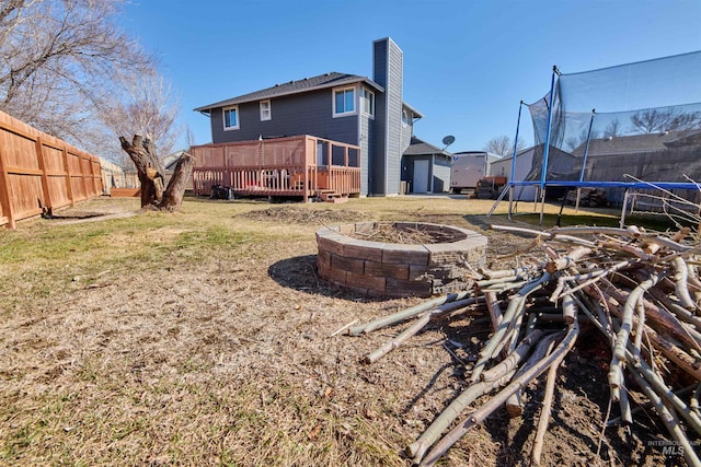 rear view of house featuring a fenced backyard, a chimney, a fire pit, a deck, and a trampoline