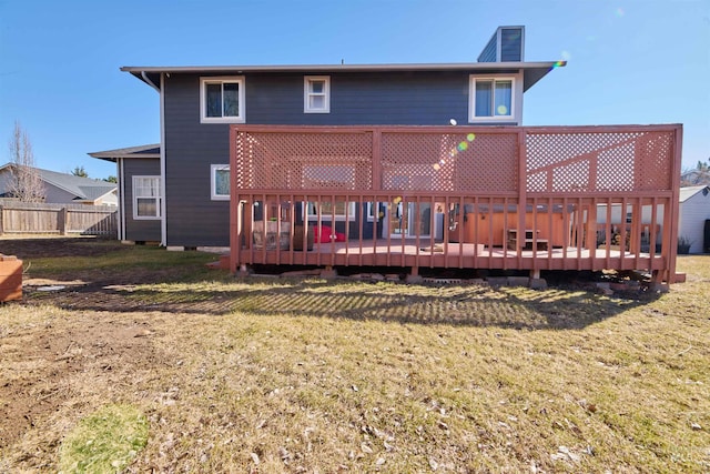 back of property with a wooden deck, a lawn, and fence