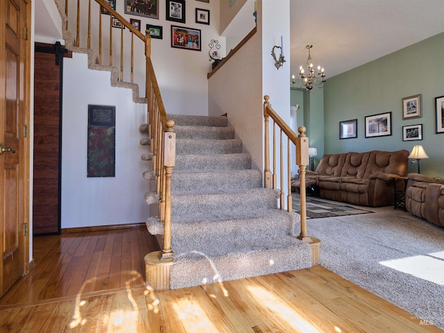 stairway with a barn door, baseboards, a notable chandelier, and hardwood / wood-style flooring