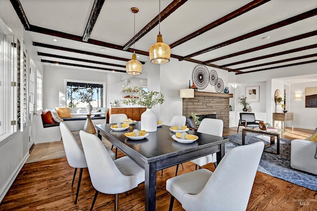 dining space featuring a stone fireplace, hardwood / wood-style floors, and beam ceiling