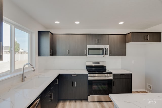 kitchen with stainless steel appliances, light stone countertops, sink, and light wood-type flooring