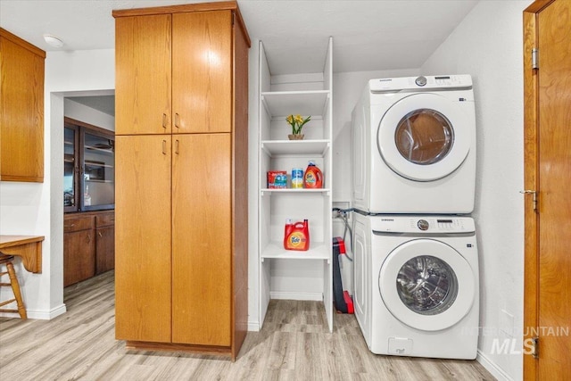 laundry area with stacked washer / dryer, baseboards, cabinet space, and light wood finished floors