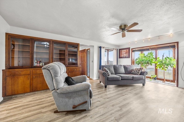 living room featuring light wood-type flooring, ceiling fan, and a textured ceiling