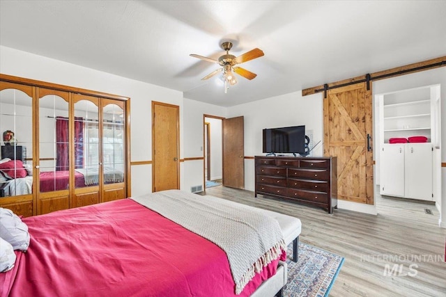 bedroom featuring ceiling fan, a barn door, and wood finished floors