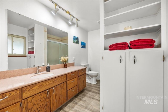 bathroom featuring toilet, wood finished floors, a shower stall, and vanity