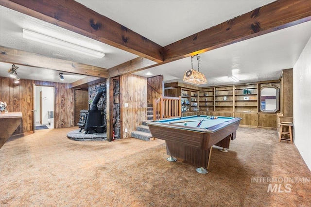 rec room with wooden walls, billiards, carpet flooring, beam ceiling, and a wood stove