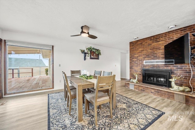 dining area featuring a ceiling fan, a fireplace, a textured ceiling, and wood finished floors