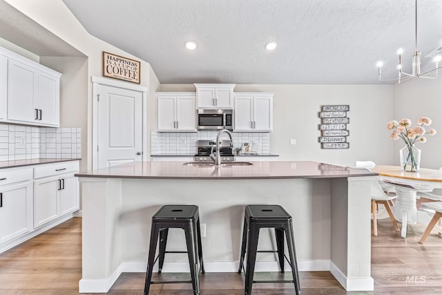 10255 W Gladiola St, Star, ID 83669 - kitchen featuring stainless steel microwave, a kitchen breakfast bar, a textured ceiling, white cabinets, and decorative backsplash