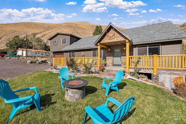 back of house with an outdoor fire pit, a deck with mountain view, and a lawn