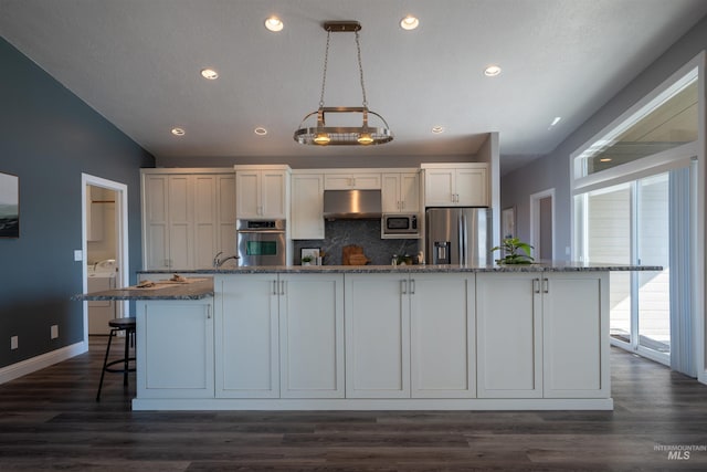 kitchen featuring dark wood-type flooring, dark stone countertops, under cabinet range hood, and stainless steel appliances