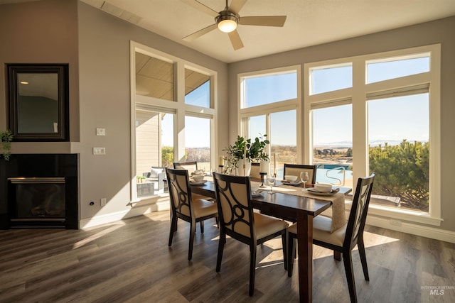 dining area featuring a glass covered fireplace, dark wood-type flooring, a ceiling fan, and baseboards