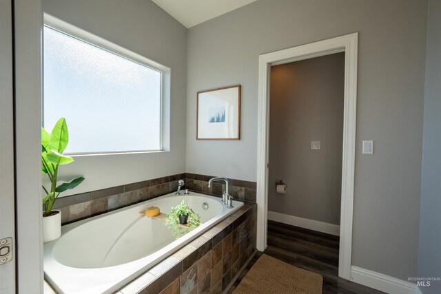 full bathroom with a wealth of natural light, a bath, baseboards, and wood finished floors