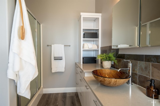 full bathroom featuring a stall shower, backsplash, wood finished floors, baseboards, and vanity