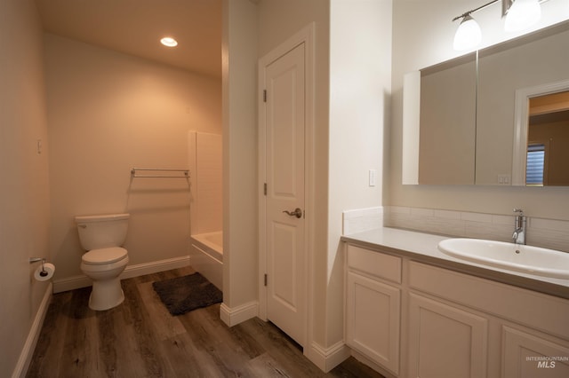 full bath with baseboards, toilet, a tub to relax in, wood finished floors, and vanity