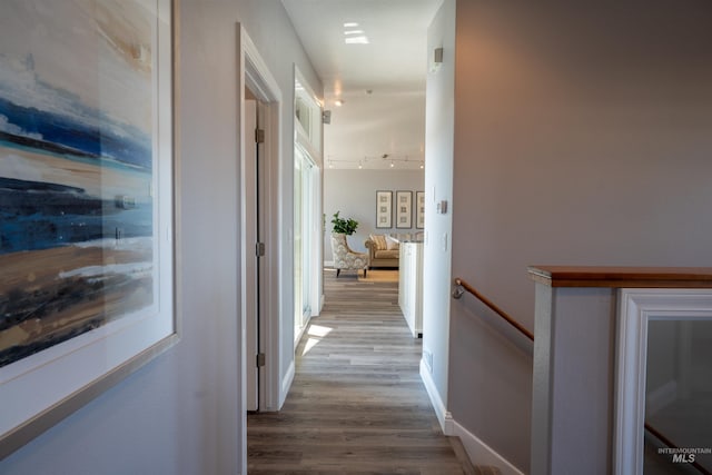 hall with wood finished floors, an upstairs landing, baseboards, and track lighting