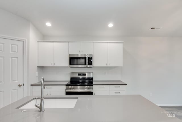 kitchen with appliances with stainless steel finishes, visible vents, white cabinetry, and tasteful backsplash