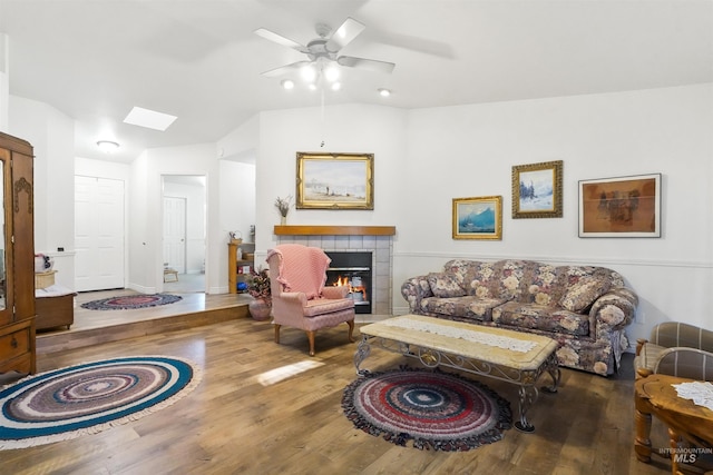 living area featuring a ceiling fan, lofted ceiling with skylight, wood finished floors, and a tile fireplace