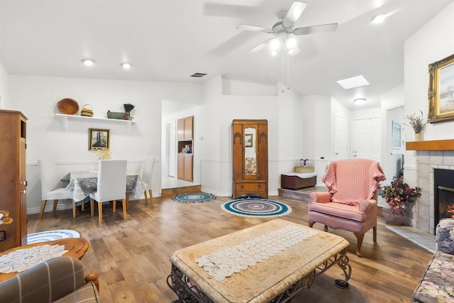 living area with visible vents, a ceiling fan, wood finished floors, and vaulted ceiling with skylight