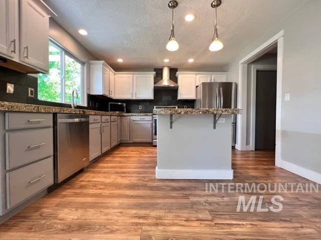 kitchen with light hardwood / wood-style flooring, wall chimney exhaust hood, a textured ceiling, a kitchen island, and stainless steel appliances