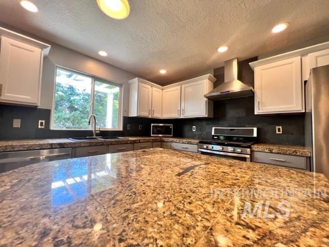 kitchen with wall chimney exhaust hood, a textured ceiling, stainless steel appliances, sink, and white cabinets