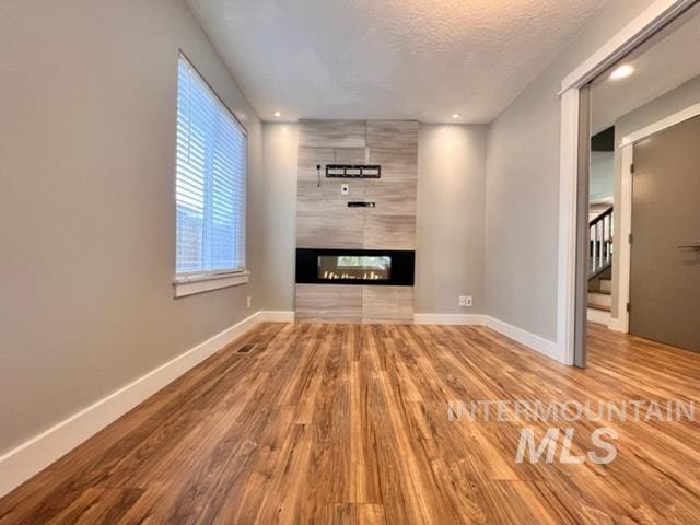 unfurnished living room with a multi sided fireplace, a textured ceiling, and hardwood / wood-style flooring