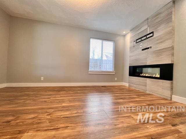 unfurnished living room featuring a multi sided fireplace, hardwood / wood-style floors, and a textured ceiling