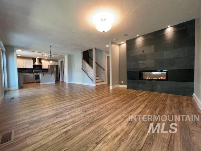 unfurnished living room with wood-type flooring, a textured ceiling, and a tiled fireplace