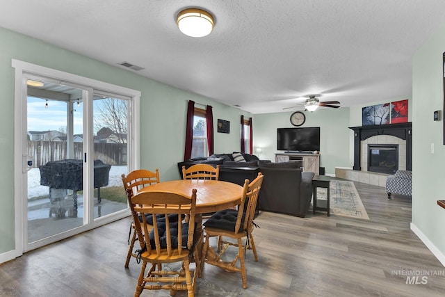 dining space with hardwood / wood-style flooring, a tile fireplace, ceiling fan, and a textured ceiling