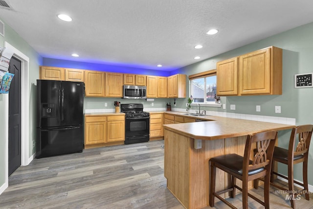 kitchen with a breakfast bar, sink, light wood-type flooring, kitchen peninsula, and black appliances