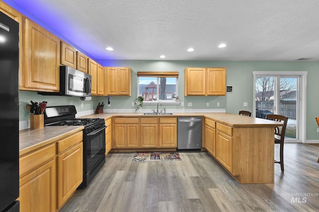 kitchen featuring sink, a breakfast bar, light hardwood / wood-style floors, black appliances, and kitchen peninsula