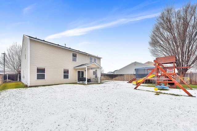 snow covered back of property with a playground