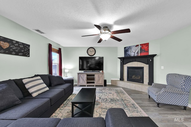 living room featuring ceiling fan, hardwood / wood-style flooring, a tile fireplace, and a textured ceiling